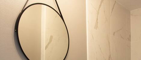 Un baño moderno con un espejo redondo, un lavabo blanco y un mueble de tocador oscuro.