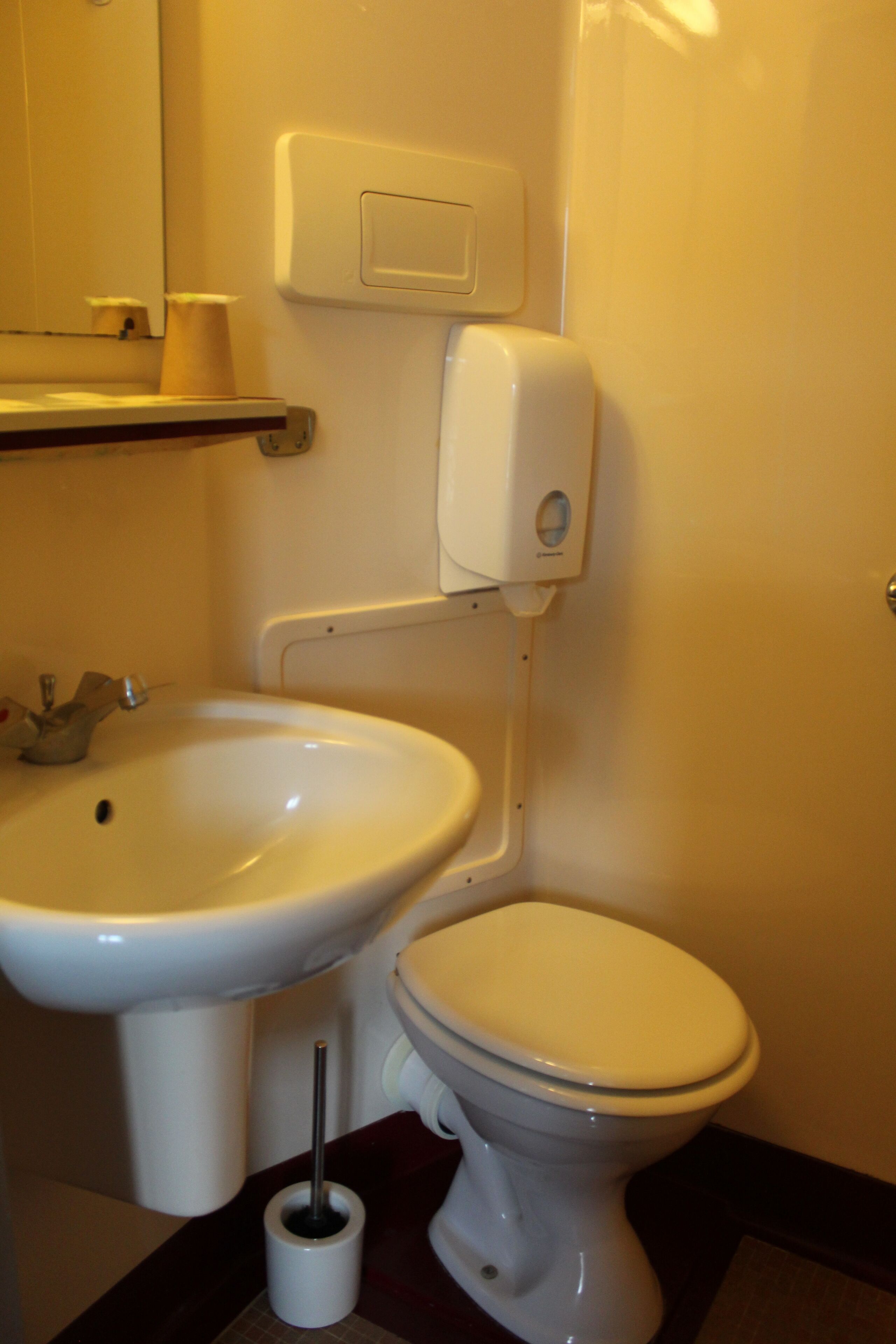 A bathroom with a sink, toilet, and a soap dispenser on the wall.
