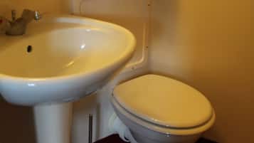 A bathroom with a sink, toilet, and a soap dispenser on the wall.