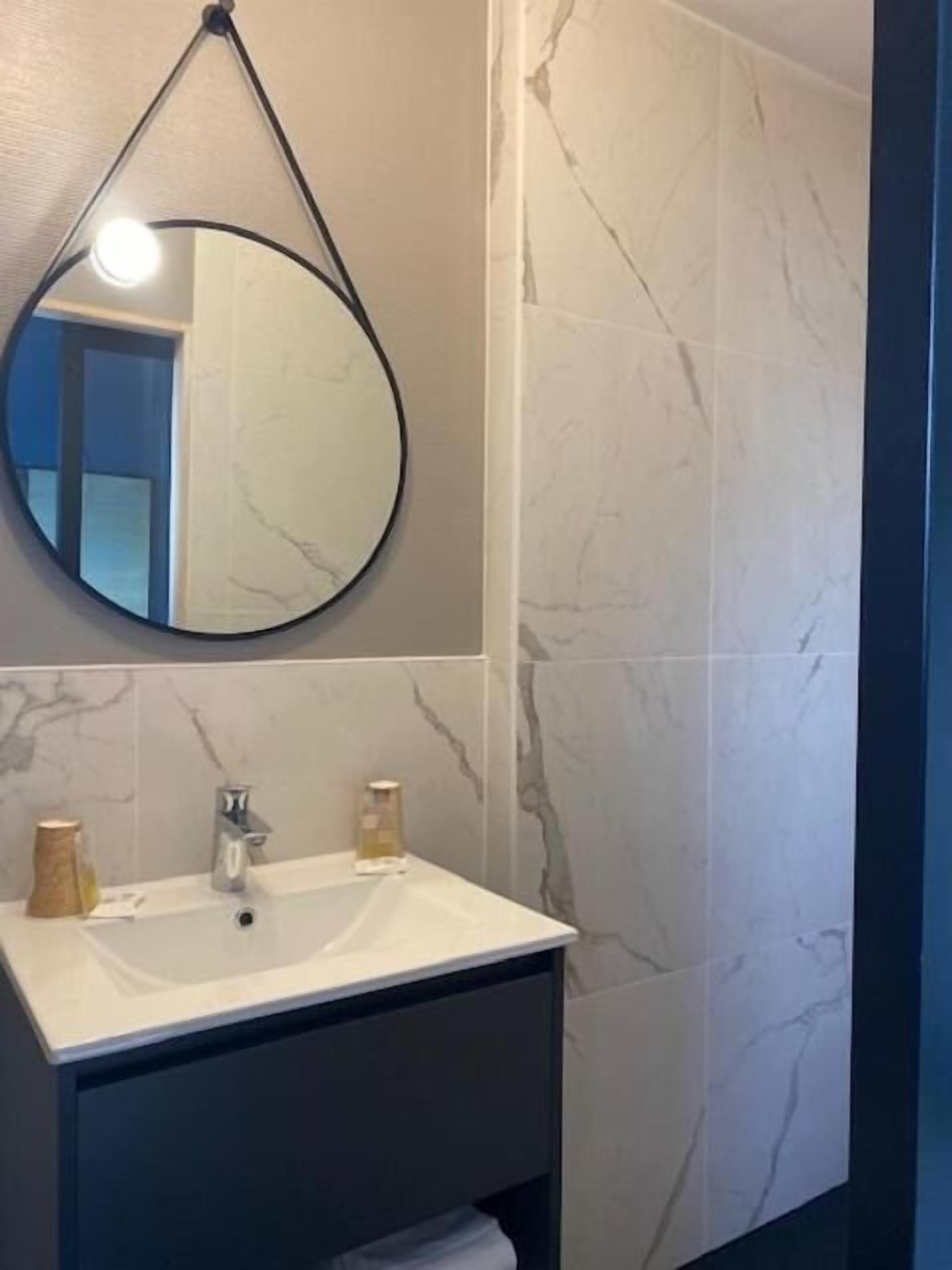A bathroom with a round mirror, a white sink, and marble-patterned walls.