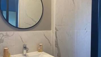 A bathroom with a round mirror, a white sink, and marble-patterned walls.