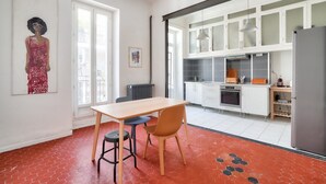 A modern kitchen with white cabinets, a built-in oven, and a refrigerator. There is a dining table with two chairs in the foreground.
