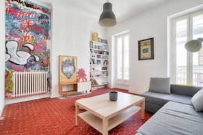 Una sala de estar con piso de ladrillo rojo, un sofá gris, una mesa de centro de madera, una estantería y un radiador.