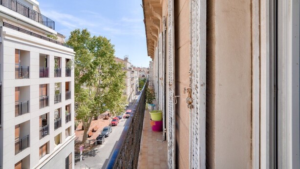 A balcony with a view of a street lined with parked cars and trees.