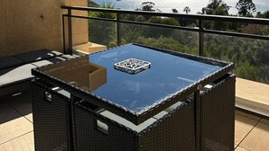 A balcony with a glass-top table, wicker furniture, and a view of the ocean.
