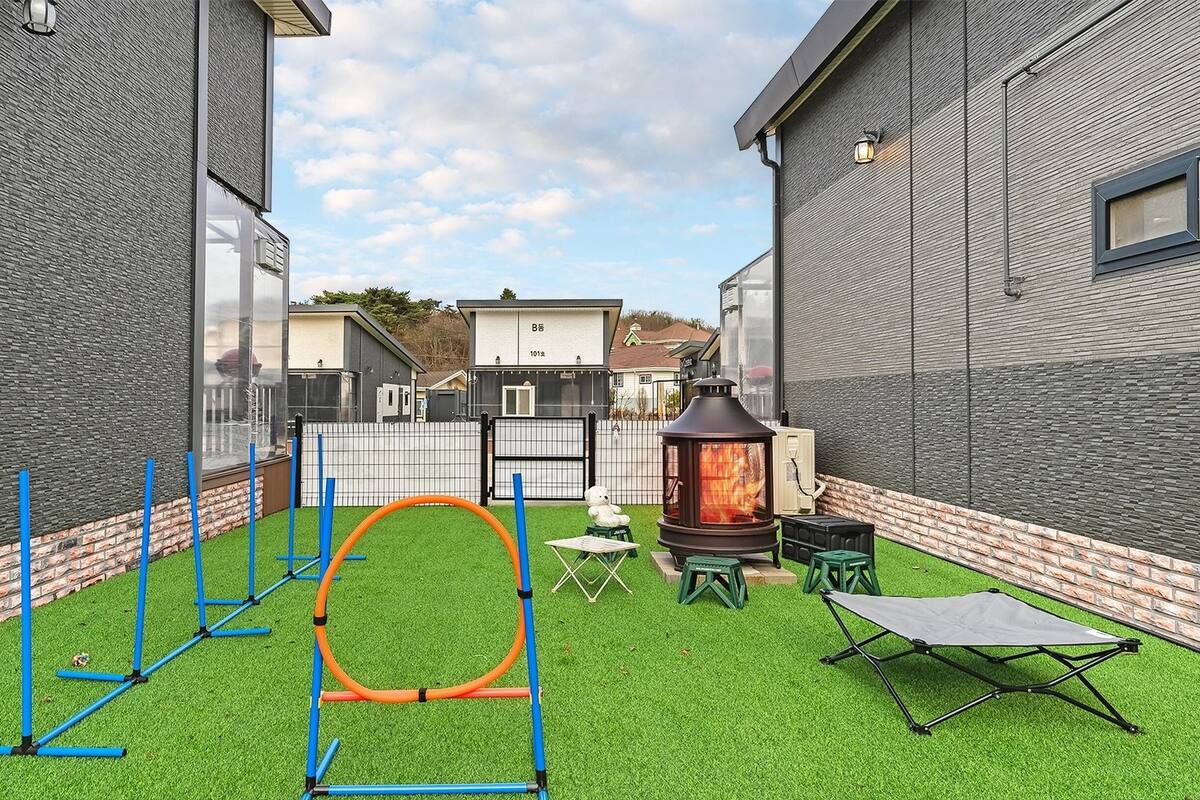 Un jardin avec une pelouse artificielle, un cerceau en métal, un chauffage mobile et une petite table.