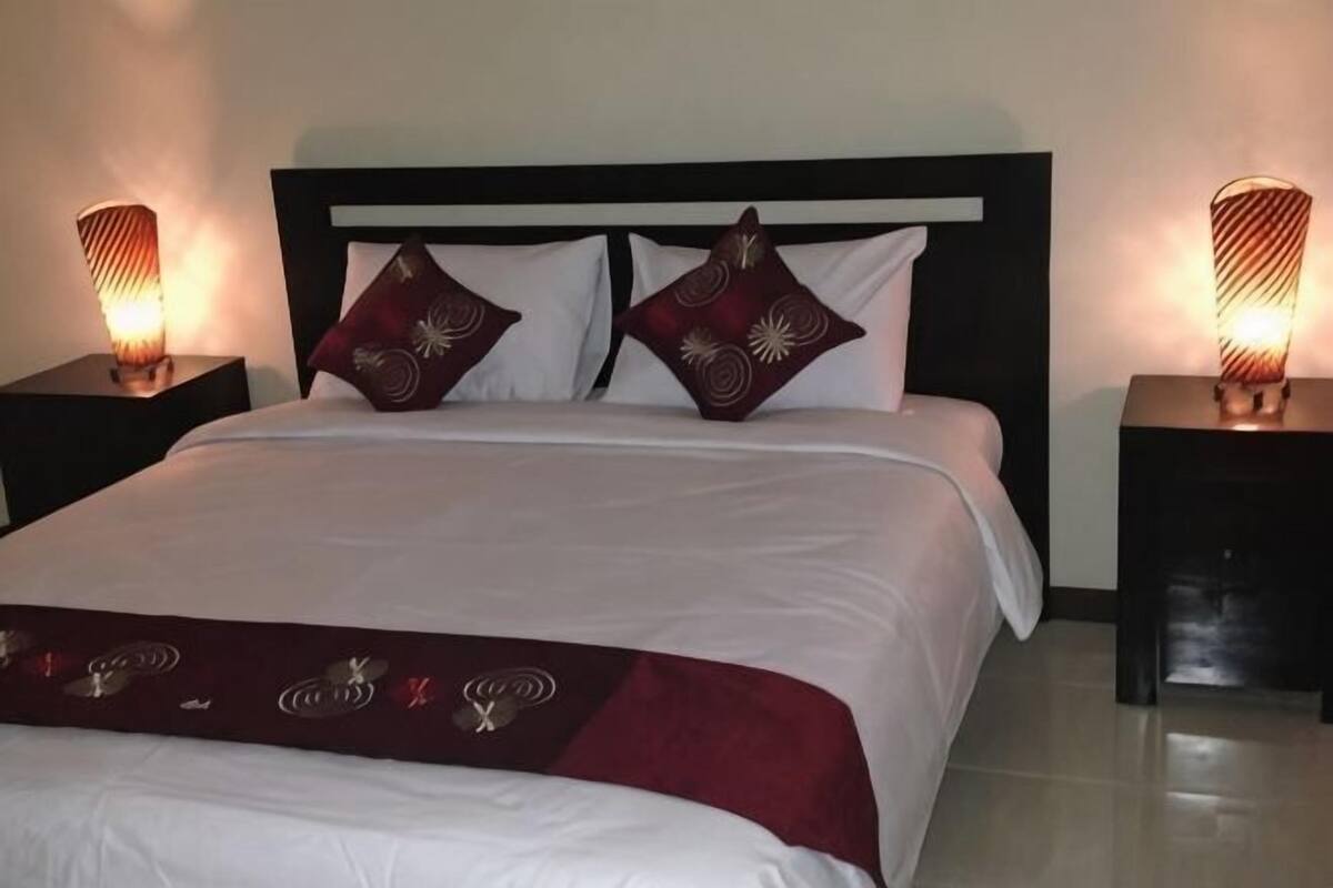A neatly made bed with a white and maroon bedspread, two decorative pillows, and two bedside lamps on nightstands.