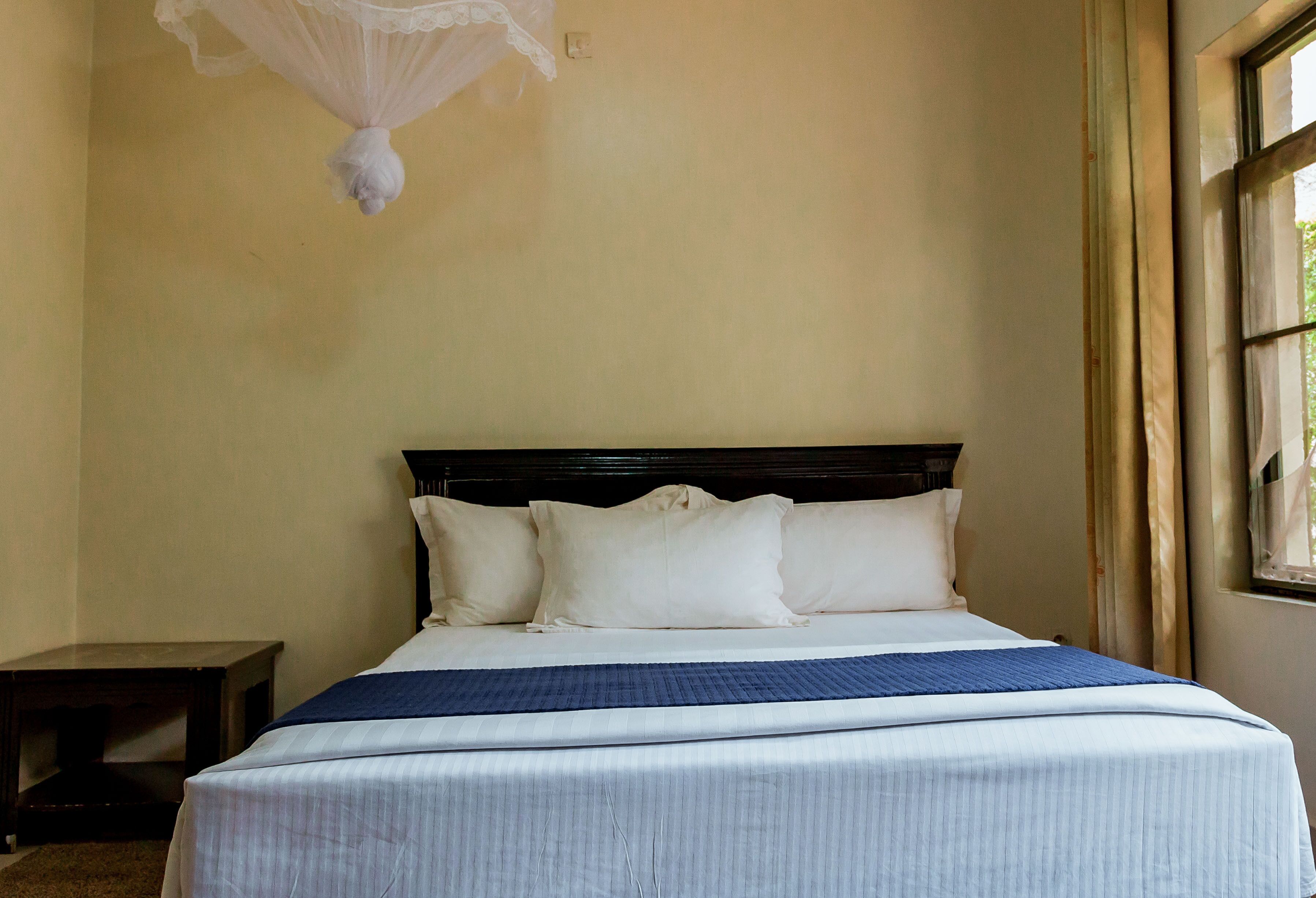 A neatly made bed with white linens and a blue blanket, a dark wooden headboard, and a small bedside table.