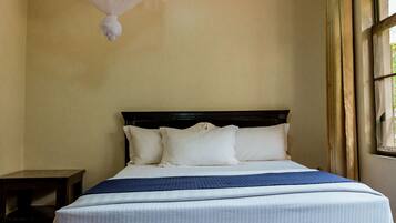 A neatly made bed with white linens and a blue blanket, a dark wooden headboard, and a small bedside table.