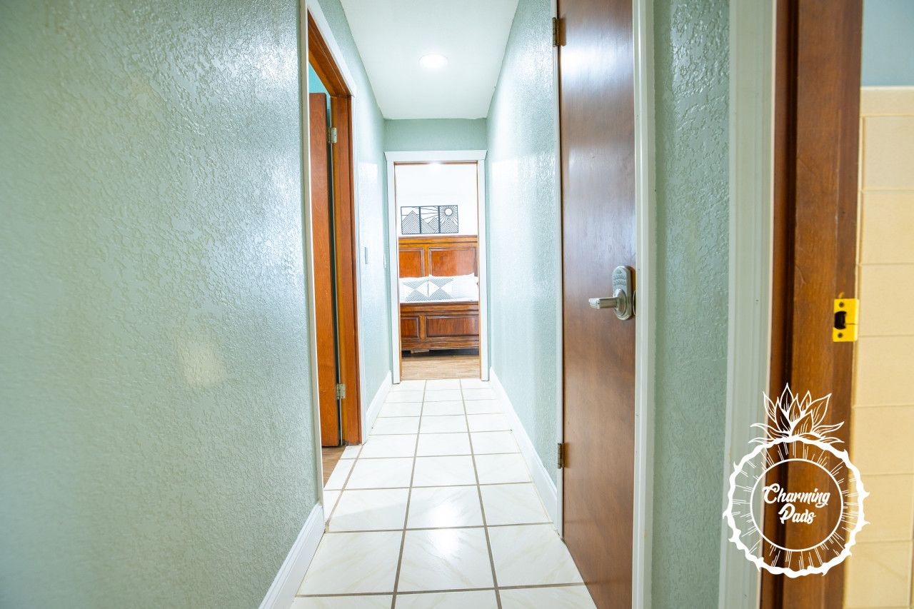 Um corredor estreito com piso de azulejos que leva a um quarto com um armário de madeira e uma janela.