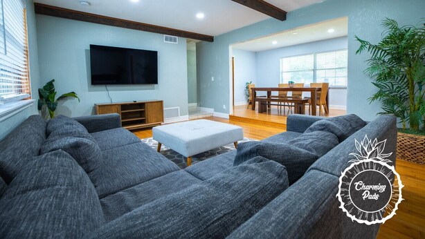 A living room with grey sofas, a flat-screen TV, wooden beams on the ceiling, and a dining area with a table and chairs. - Winter Park Charmer - Heated Pool Home - Close to everything (Winter Park)