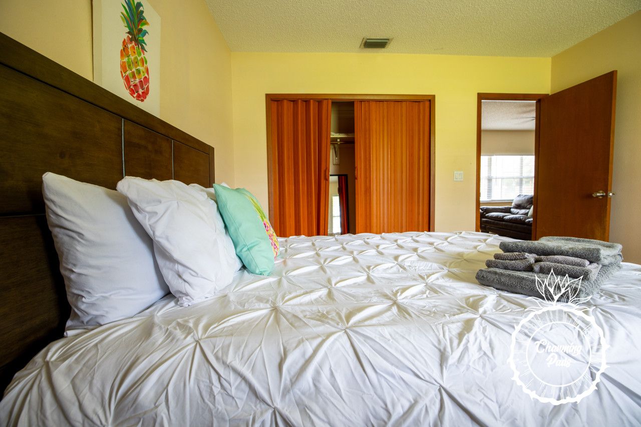 Een hotelkamer met een groot bed, witte beddengoed, een houten hoofdbord en een ananas kunstwerk aan de muur.