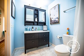A bathroom with a dark vanity, a white toilet, and a framed picture on the wall. - Winter Park Charmer - Heated Pool Home - Close to everything (Winter Park)
