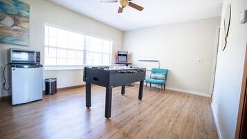 Une pièce avec une table de baby-foot, une petite kitchenette équipée d’un four à micro-ondes et un ventilateur de plafond.