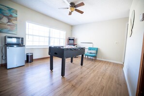 Una habitación con mesa de fútbol, una kitchenette pequeña con microondas y un ventilador de techo.