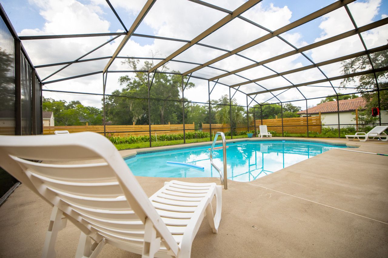 A covered outdoor swimming pool with lounge chairs and a metal frame structure.