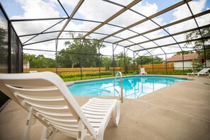 A covered outdoor swimming pool with lounge chairs and a metal frame structure.