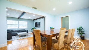 A dining area with a wooden table and wicker chairs, a grey sofa, and a television mounted on the wall. - Winter Park Charmer - Heated Pool Home - Close to everything (Winter Park)