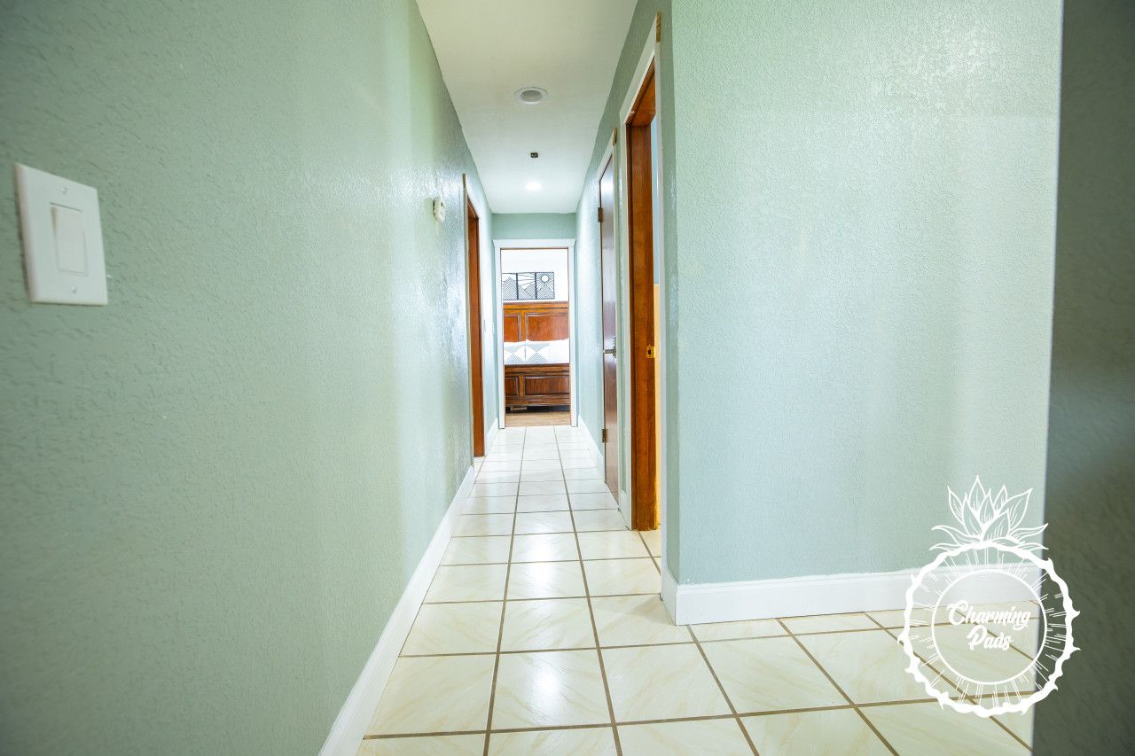 A hallway with light green walls and white tiled flooring, leading to a kitchen area.