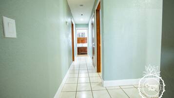 A hallway with light green walls and white tiled flooring, leading to a kitchen area.