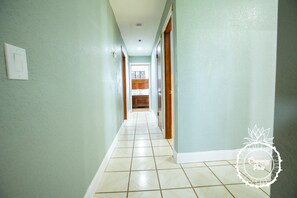 Un pasillo con paredes verde claro y suelo de baldosas blancas, que conduce a una zona de cocina.