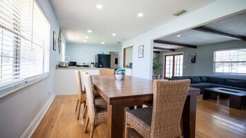 Un comedor amplio con una mesa de madera y sillas de mimbre, una cocina al fondo y un área de estar con un sofá y una mesita de centro.