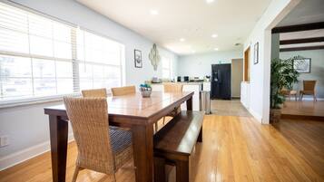 Uma sala de jantar espaçosa com mesa de madeira e cadeiras de vime, cozinha ao fundo e vista através de uma porta aberta.
