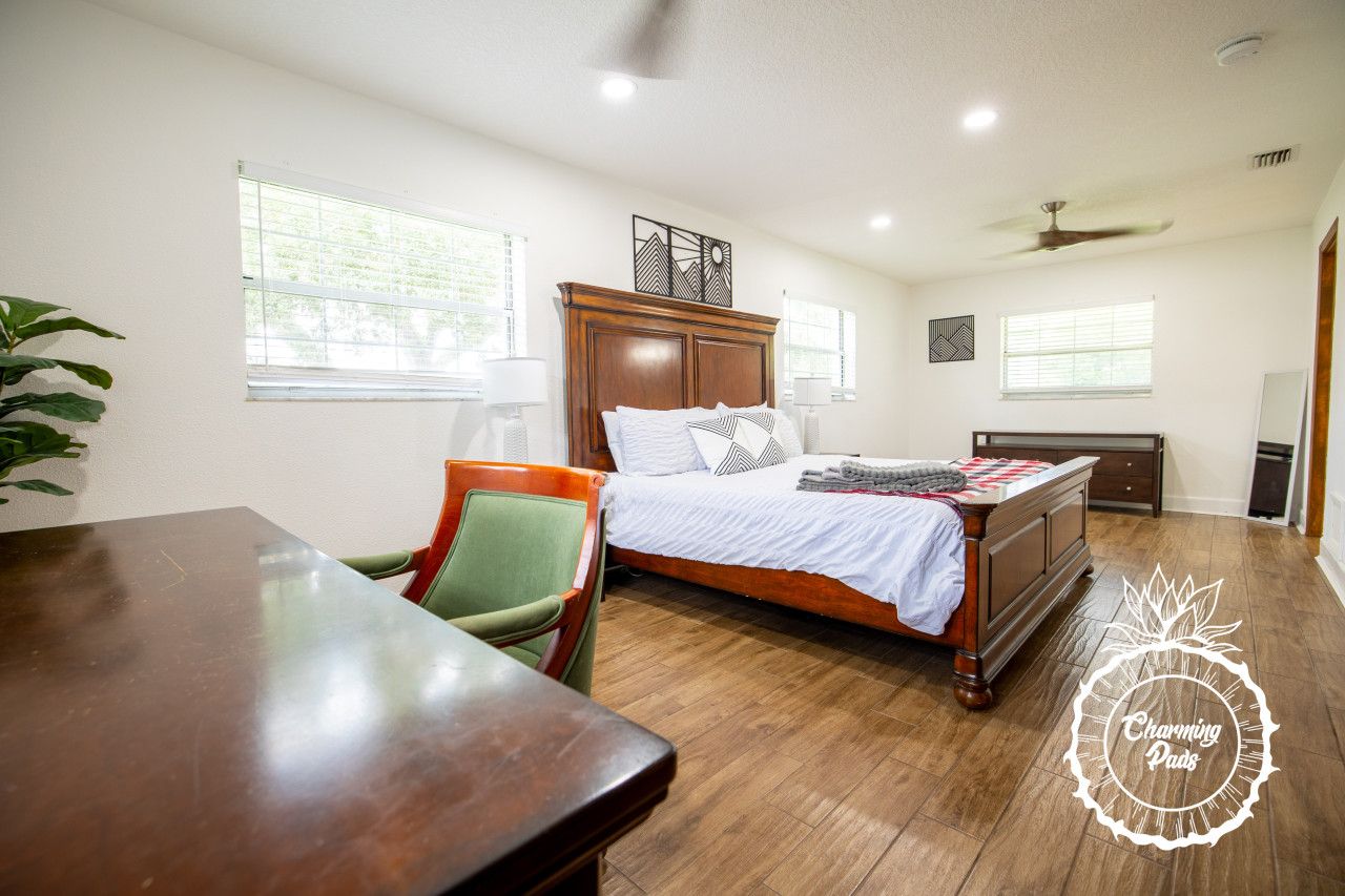 Um quarto com cama de madeira, uma cadeira verde, uma mesa de madeira e um ventilador de teto.