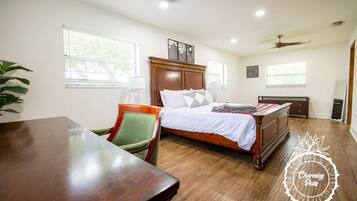 Um quarto com cama de madeira, uma cadeira verde, uma mesa de madeira e um ventilador de teto.