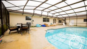 Piscina interna com um terraço coberto, incluindo uma mesa e cadeiras, e um espaço de descanso à beira da piscina.