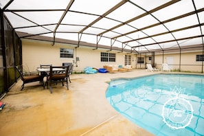 Una piscina interior con un porche cubierto, que incluye una mesa y sillas, y un área de descanso junto a la piscina.