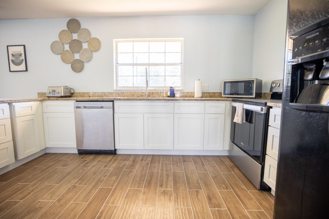 A modern kitchen with white cabinets, a dishwasher, a microwave, and a refrigerator.