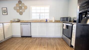 A modern kitchen with white cabinets, a dishwasher, a microwave, and a refrigerator.