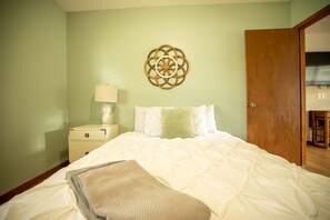 A bedroom with a bed, a nightstand, a wall decoration, and a door.