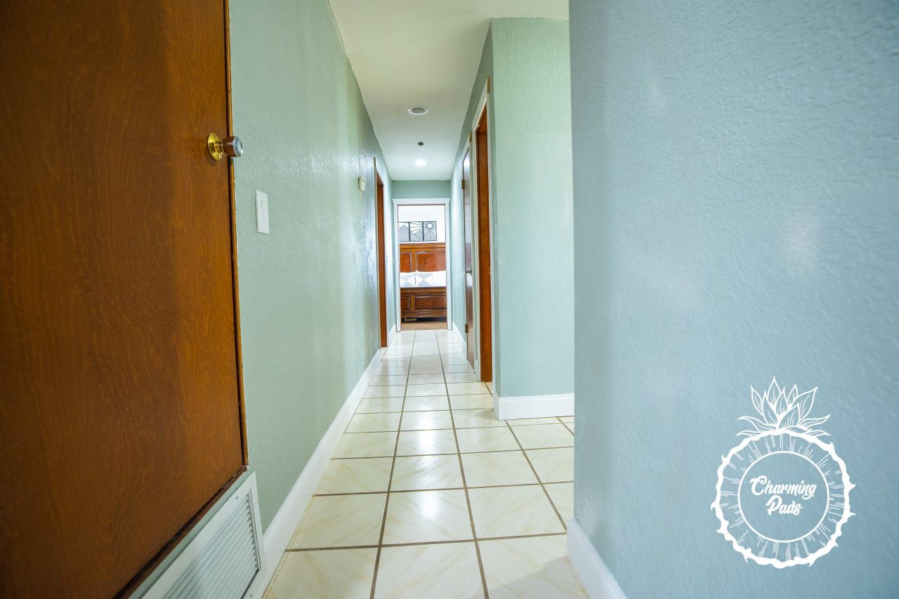 Um corredor com uma porta de madeira à esquerda, chão de azulejos e paredes verde-claras.