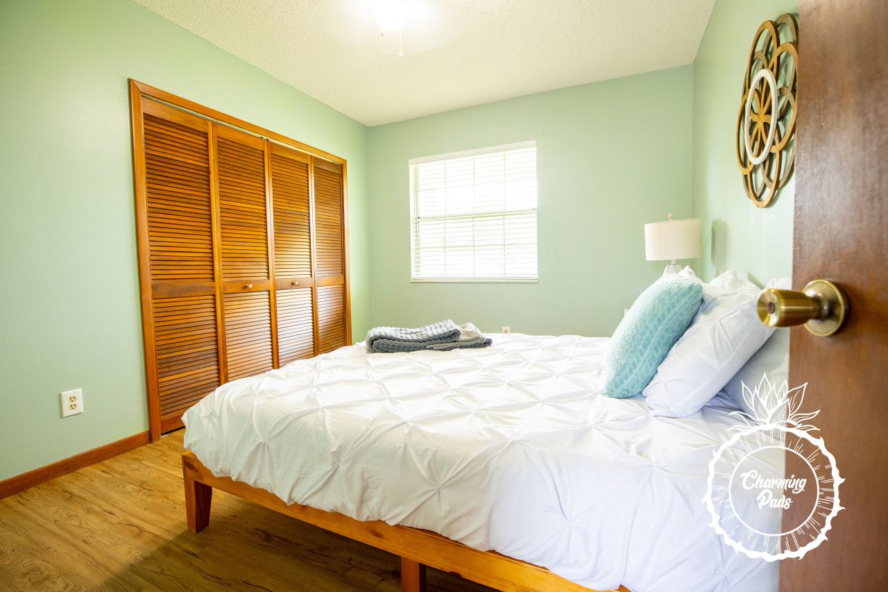 Quarto com cama, janela, porta e um objeto decorativo fixado na parede.