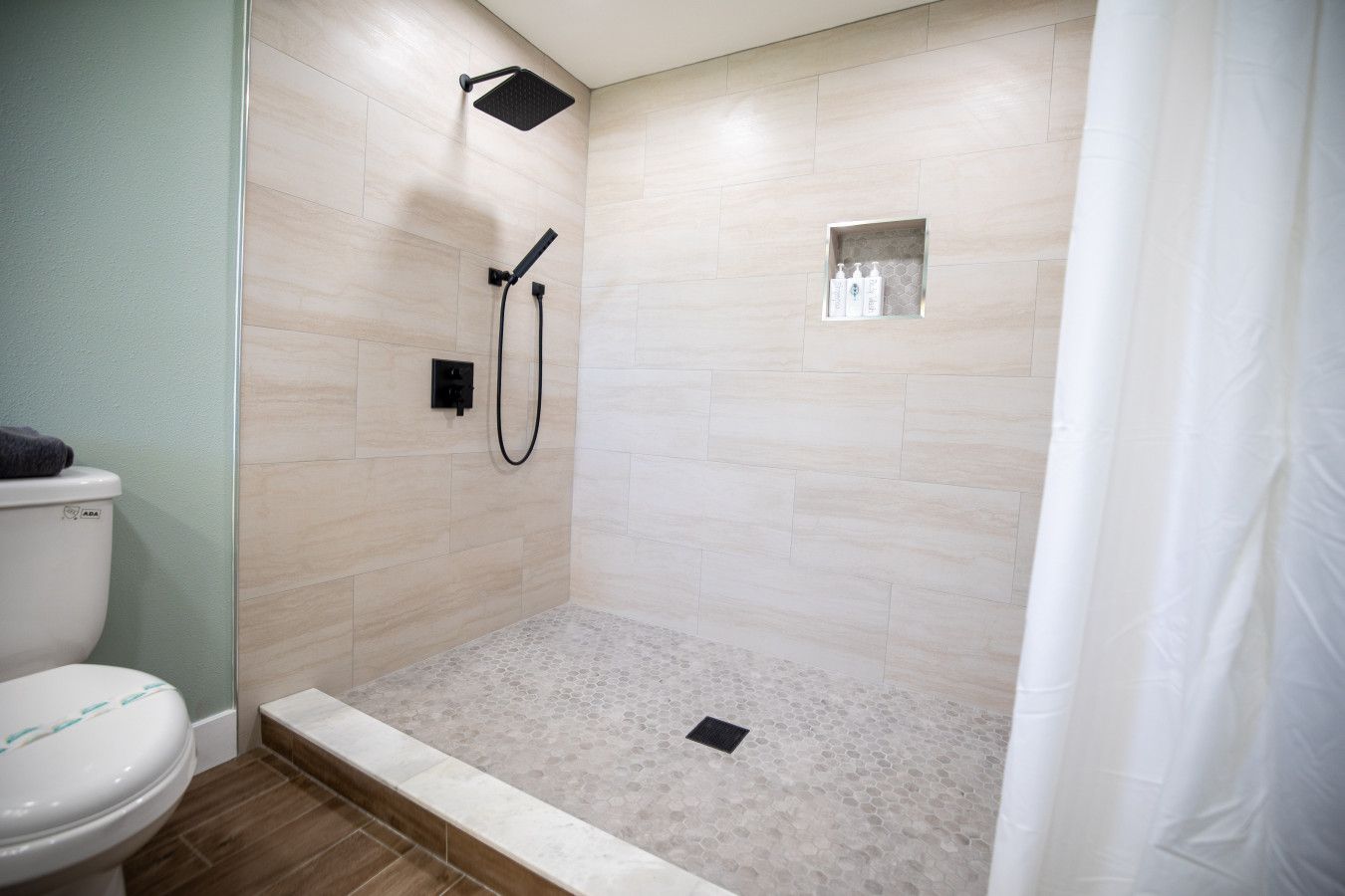 A shower area with a tiled floor, a handheld showerhead, and a small shelf with toiletries.