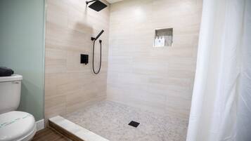 A shower area with a tiled floor, a handheld showerhead, and a small shelf with toiletries.