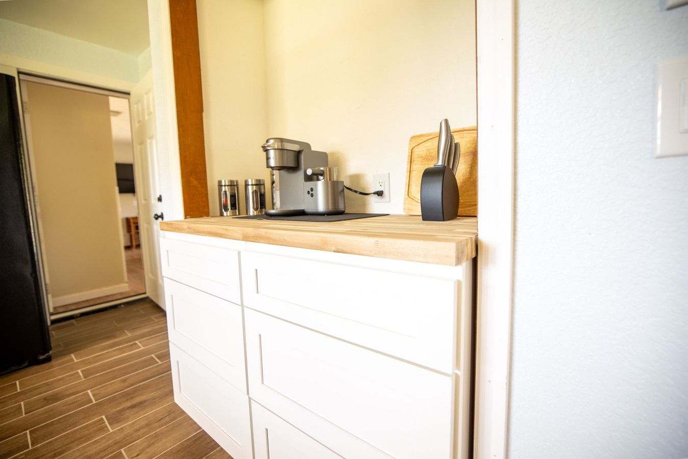 A kitchen with white cabinets, a wooden countertop, a coffee maker, and a toaster.
