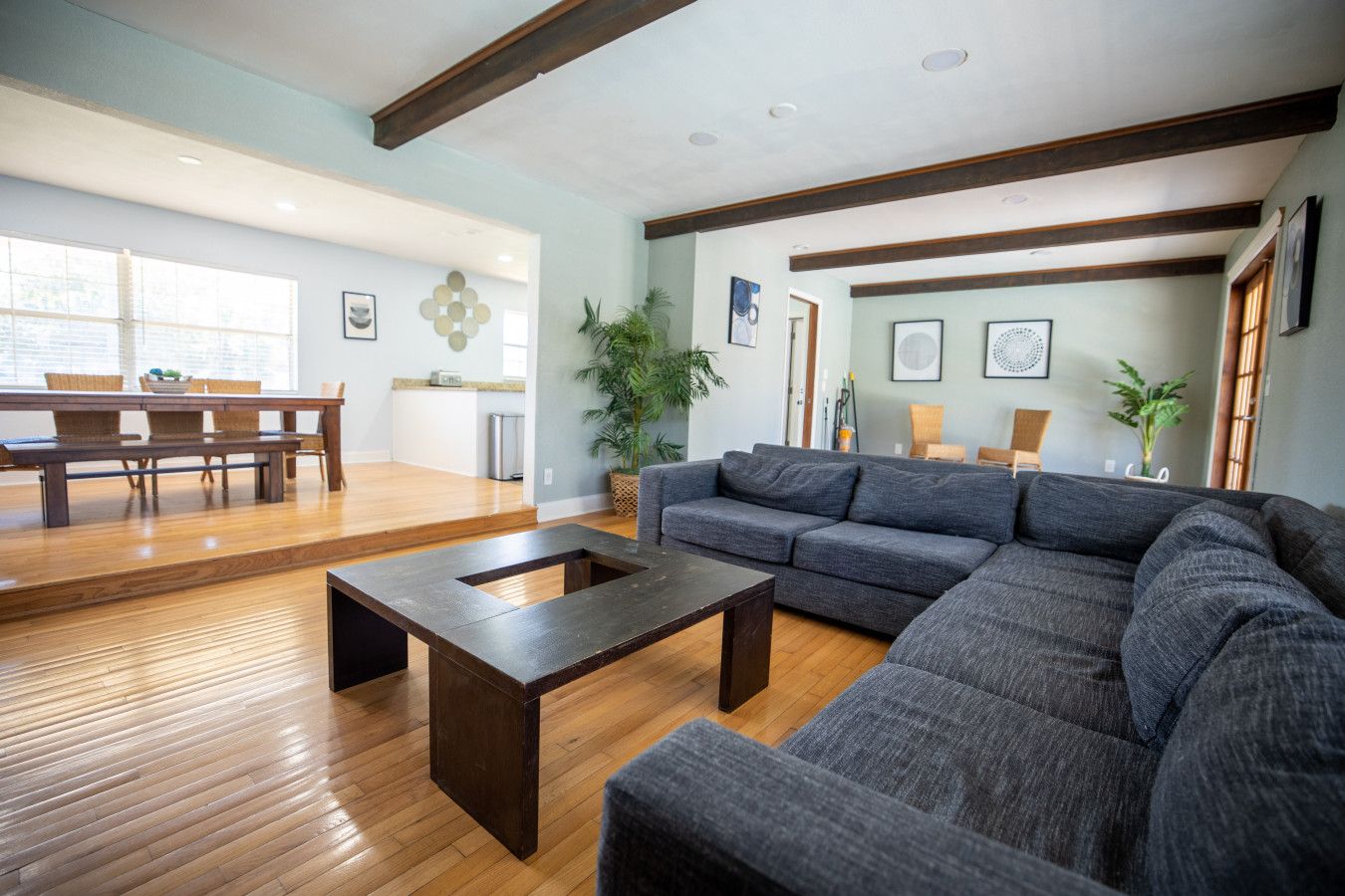 Uma sala de estar ampla com uma mesa de centro de madeira escura, um sofá modular cinza e piso de madeira.