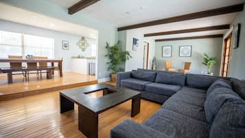 A spacious living room with a dark wooden coffee table, a grey sectional sofa, and wooden flooring.