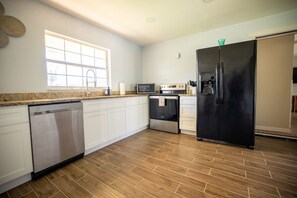 A kitchen with white cabinets, a stainless steel dishwasher, a black refrigerator, a microwave, and a stove.