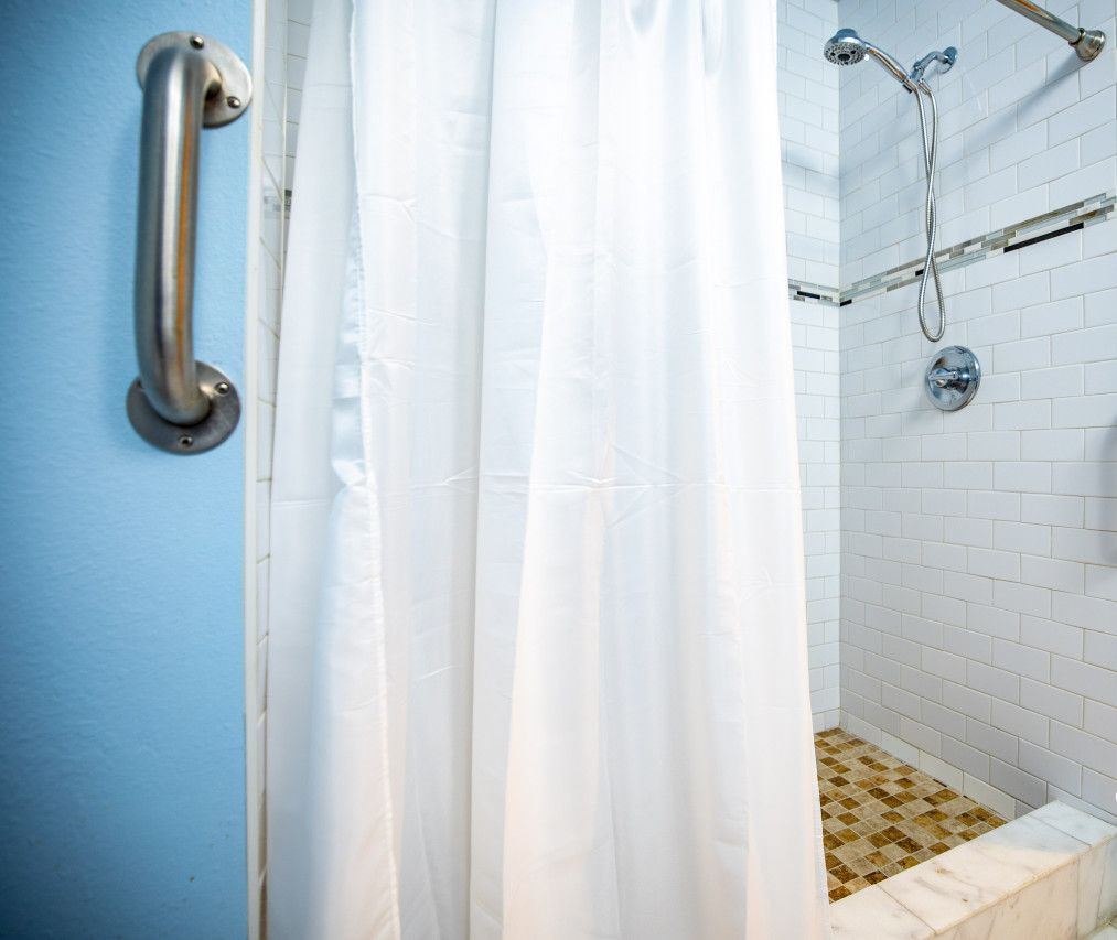 Um banheiro com paredes revestidas de azulejos brancos, um chuveiro com porta de vidro e uma cortina branca.