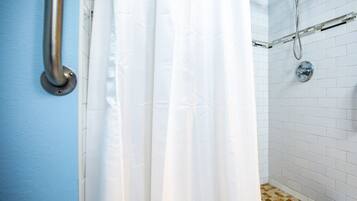 Um banheiro com paredes revestidas de azulejos brancos, um chuveiro com porta de vidro e uma cortina branca.