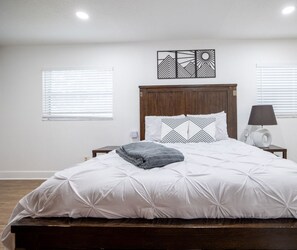 A bedroom with a wooden headboard, white bedding, a gray throw blanket, a bedside lamp, and a decorative wall piece. - Winter Park Charmer - Heated Pool Home - Close to everything (Winter Park)