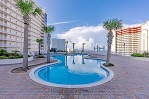 Relax by the resort pool surrounded by palm trees and lounge chairs.