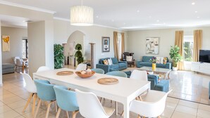 Un vaste espace de vie comprenant une table à manger, des chaises bleues et blanches, un ensemble de canapés et un téléviseur.