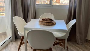 Un coin repas avec une table et des chaises, une vue sur le paysage urbain par une fenêtre et des rideaux à la fenêtre.