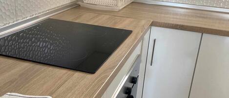 A kitchen with a black induction cooktop, white cabinets, and a wooden countertop.