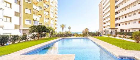 Una piscina rodeada de césped y árboles bien cuidados, con rascacielos al fondo.